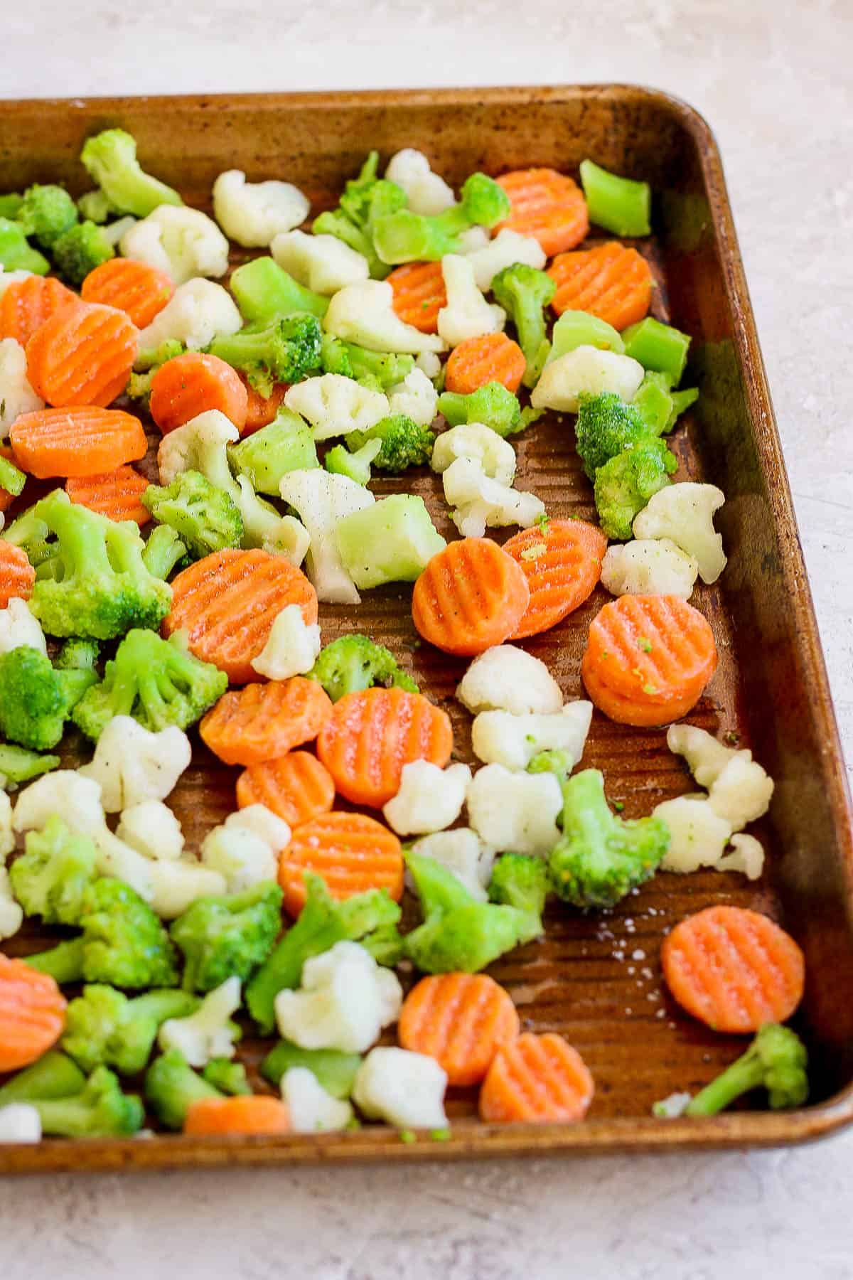 Salt and pepper on frozen veggies on a baking sheet.
