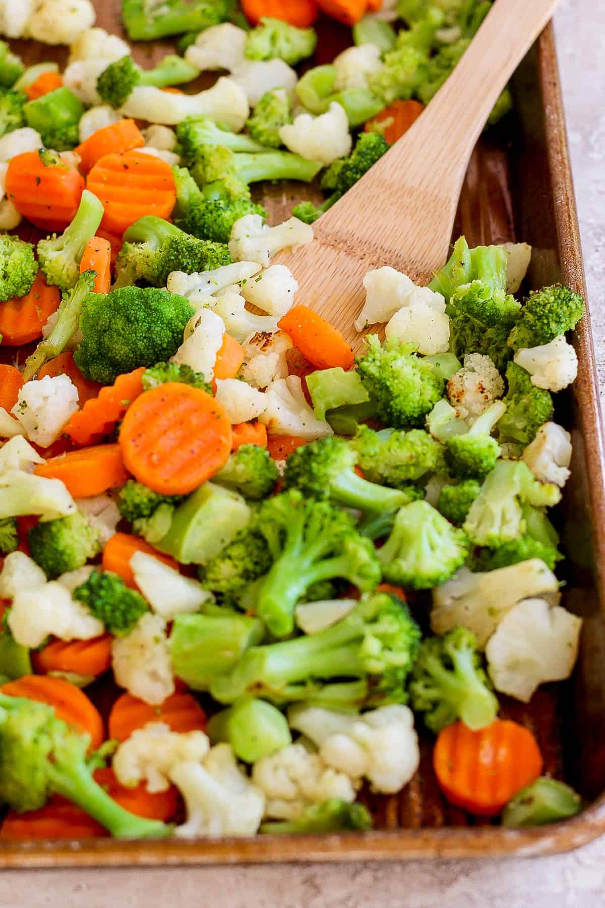 Roasted frozen veggies on a baking sheet with a wooden spoon.