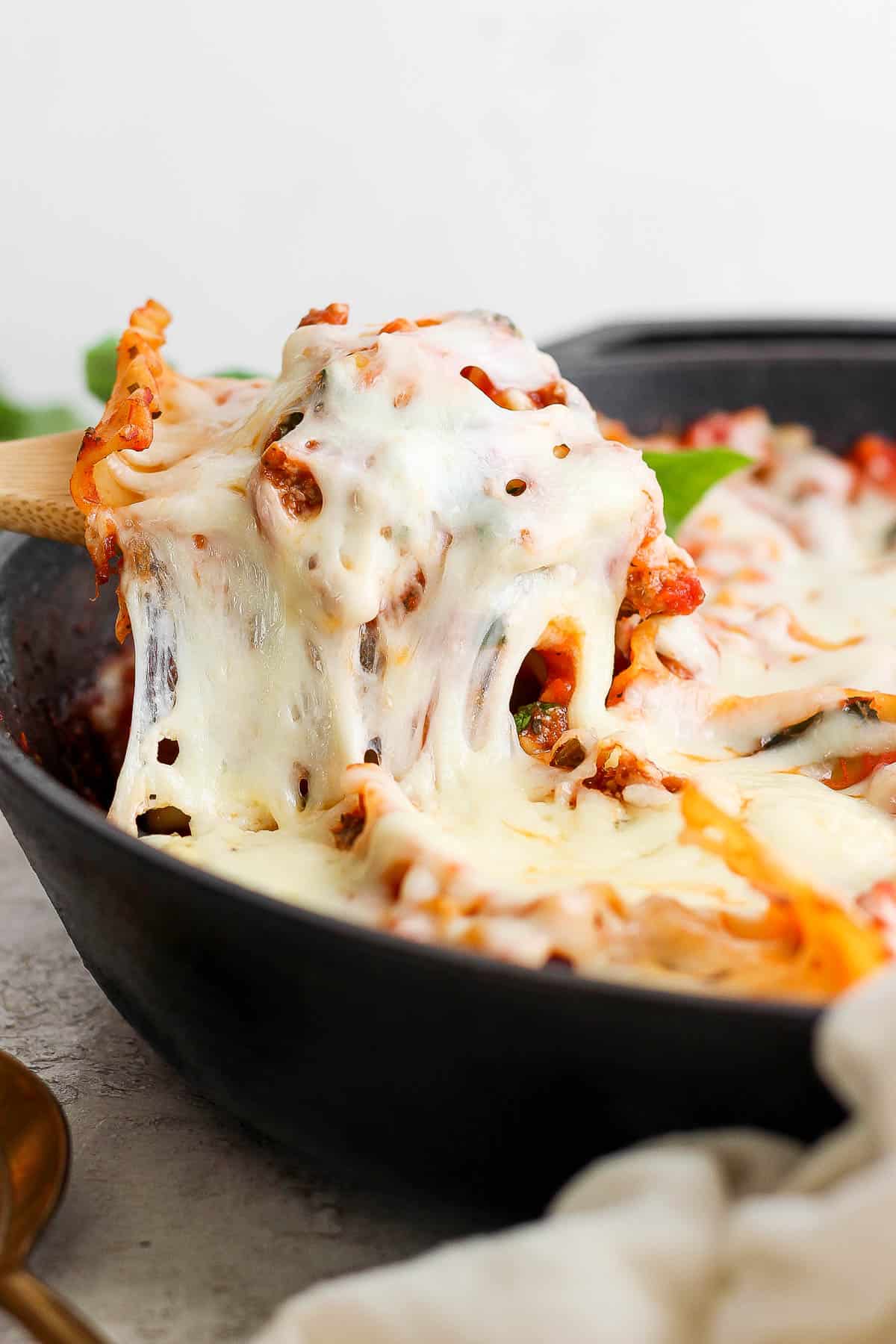 A wooden spoon pulling out a serving of lazy lasagna from the skillet.