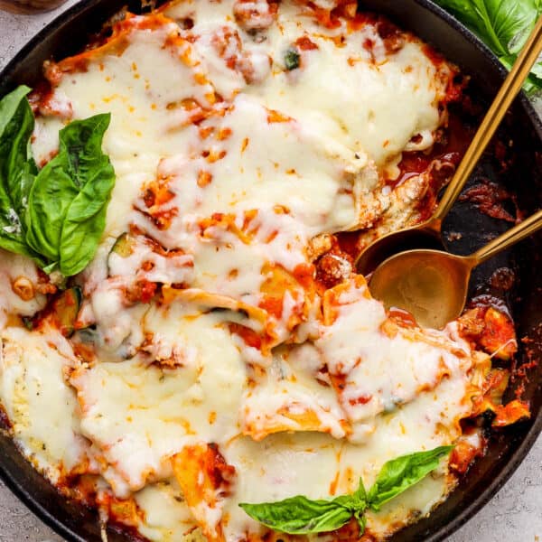 Top down shot of a cast iron skillet filled with a lazy lasagna with two spoon sticking out and fresh basil on top.