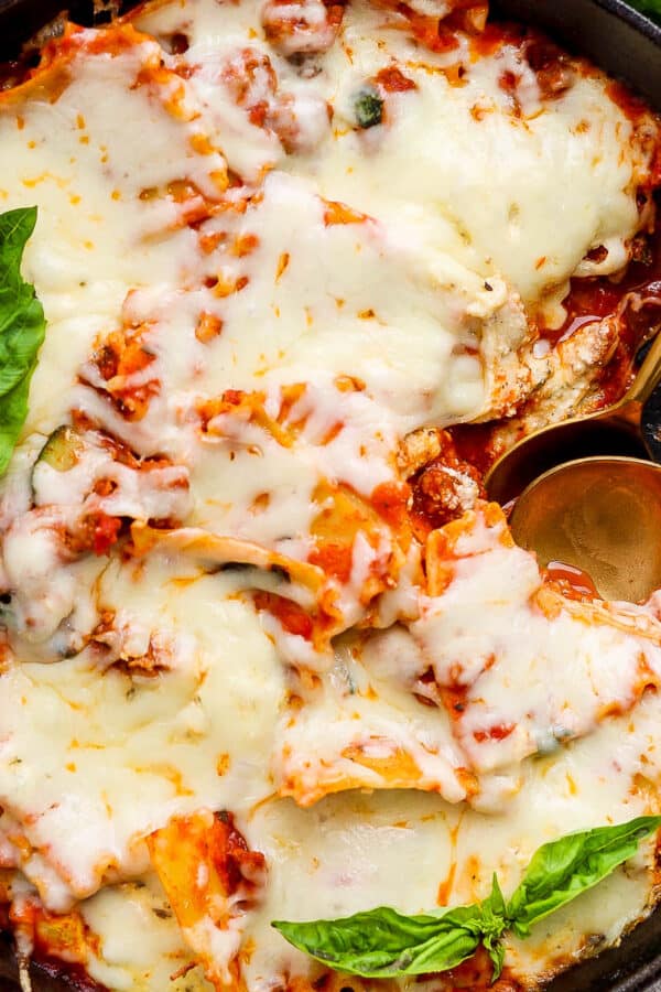 Top down shot of a cast iron skillet filled with a lazy lasagna with two spoon sticking out and fresh basil on top.