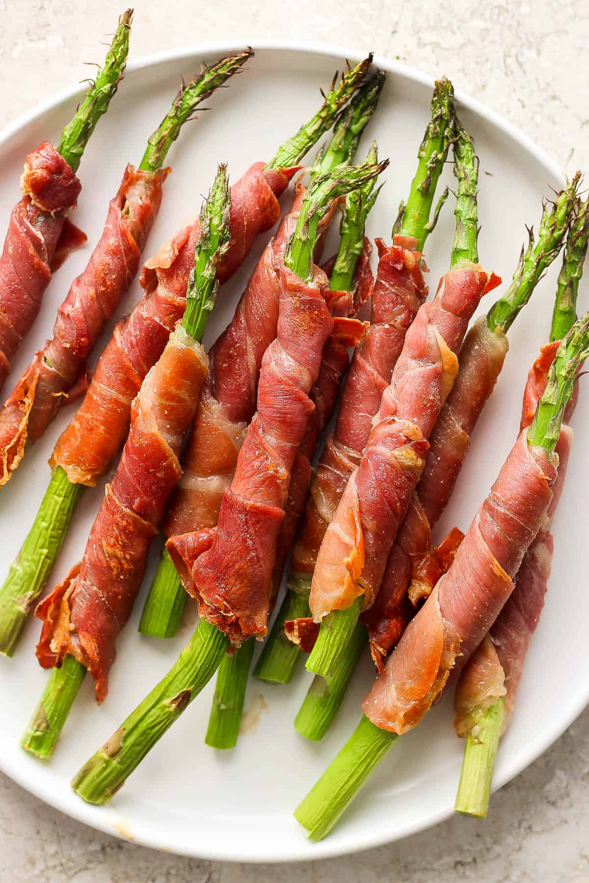 Prosciutto wrapped asparagus on a white plate.