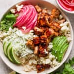Top down shot of a salmon taco bowl with rice, limes, quick pickled onions, salmon pieces, avocado and slaw.