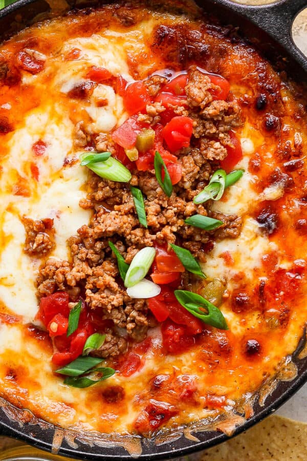 Top down shot of a small cast iron skillet filled with smoked queso and garnished with chorizo, green onions and tomatoes.