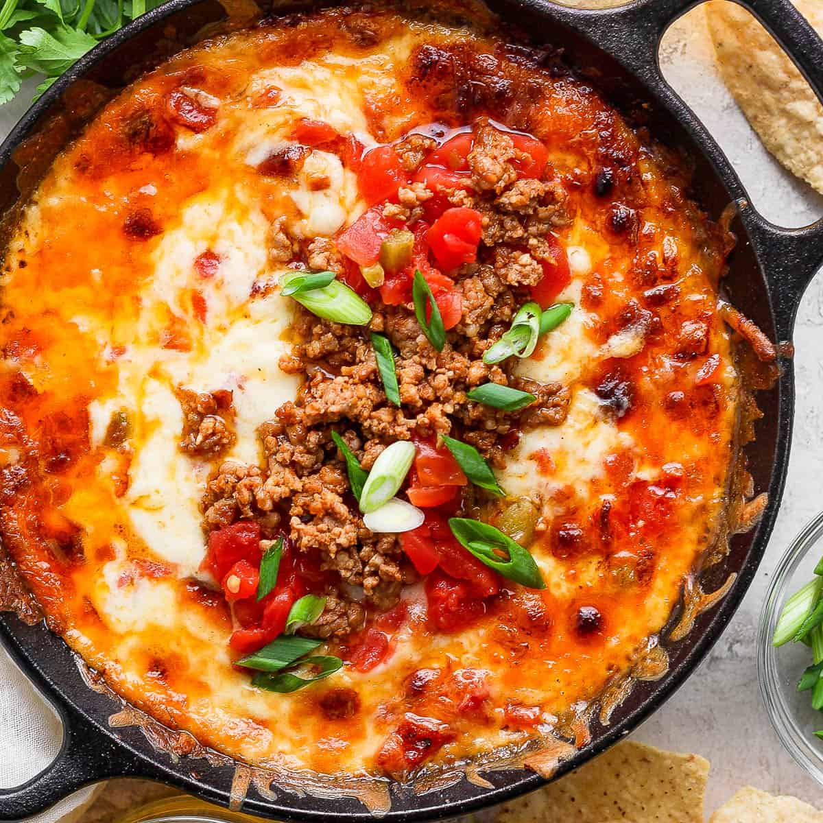 Top down shot of a small cast iron skillet filled with smoked queso and garnished with chorizo, green onions and tomatoes.