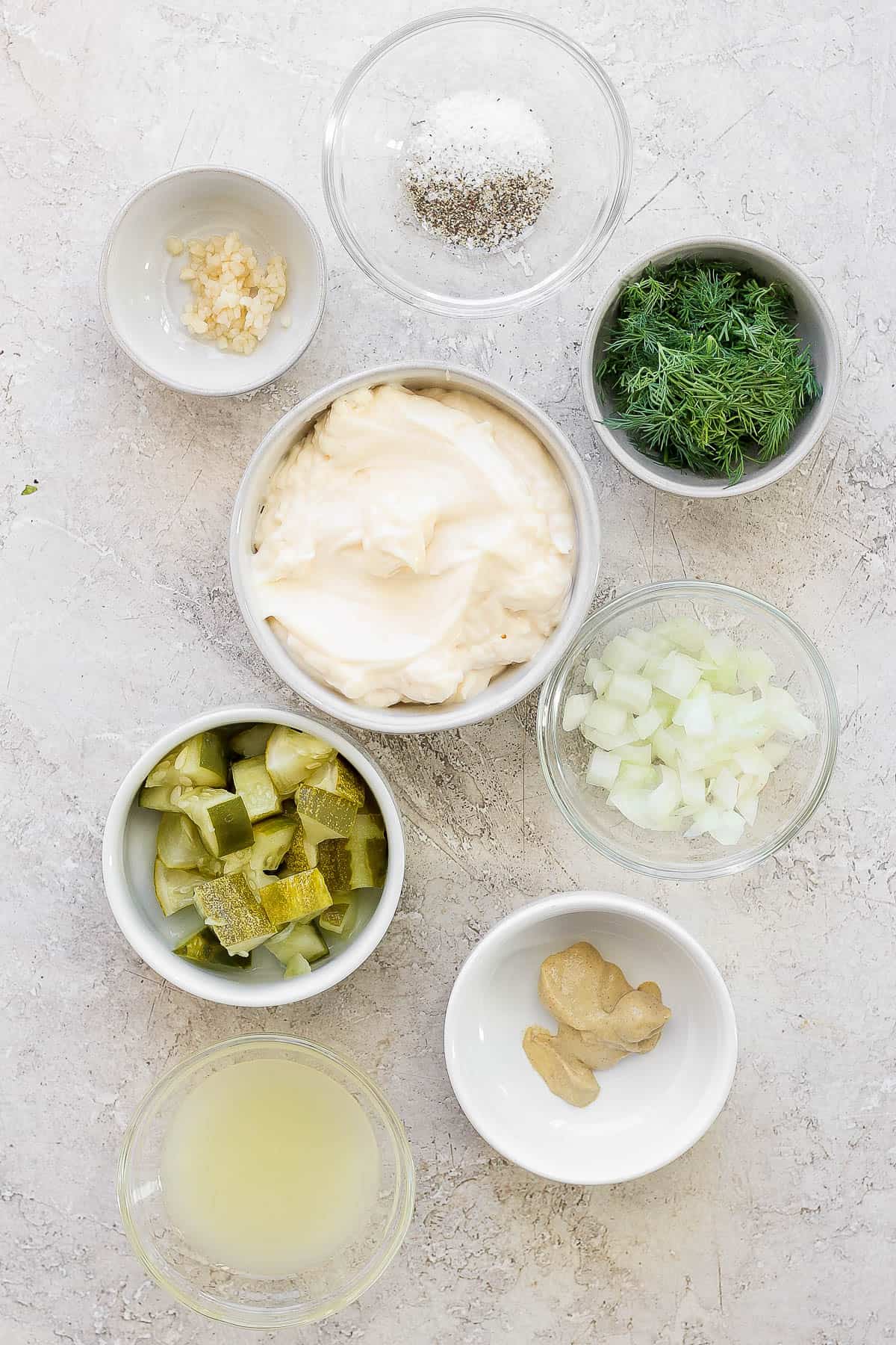 Individual bowls of lemon juice, dijon mustard, chopped pickles, onion, mayo, fresh dill, minced garlic, salt, and pepper.