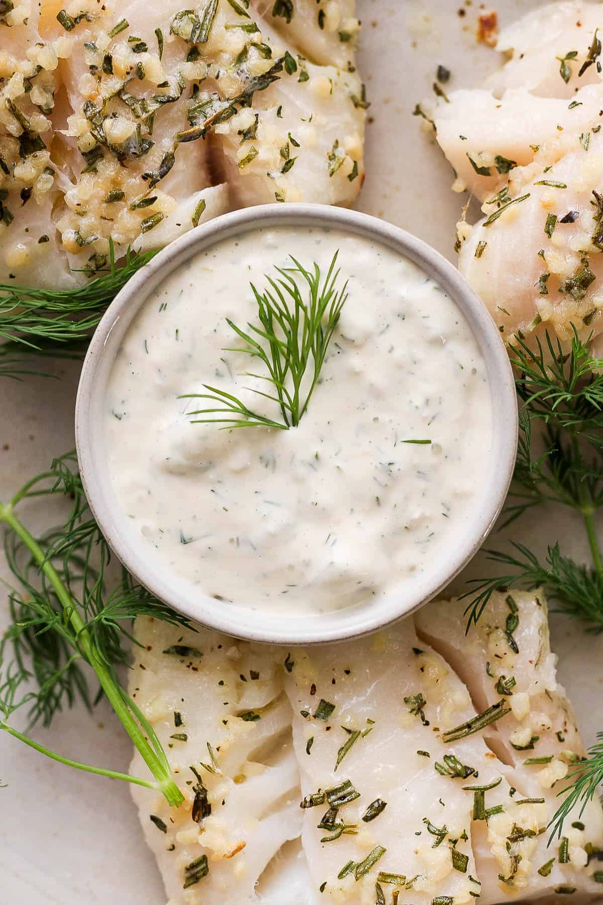A bowl of fresh tartar sauce surrounded by baked cod and fresh dill.