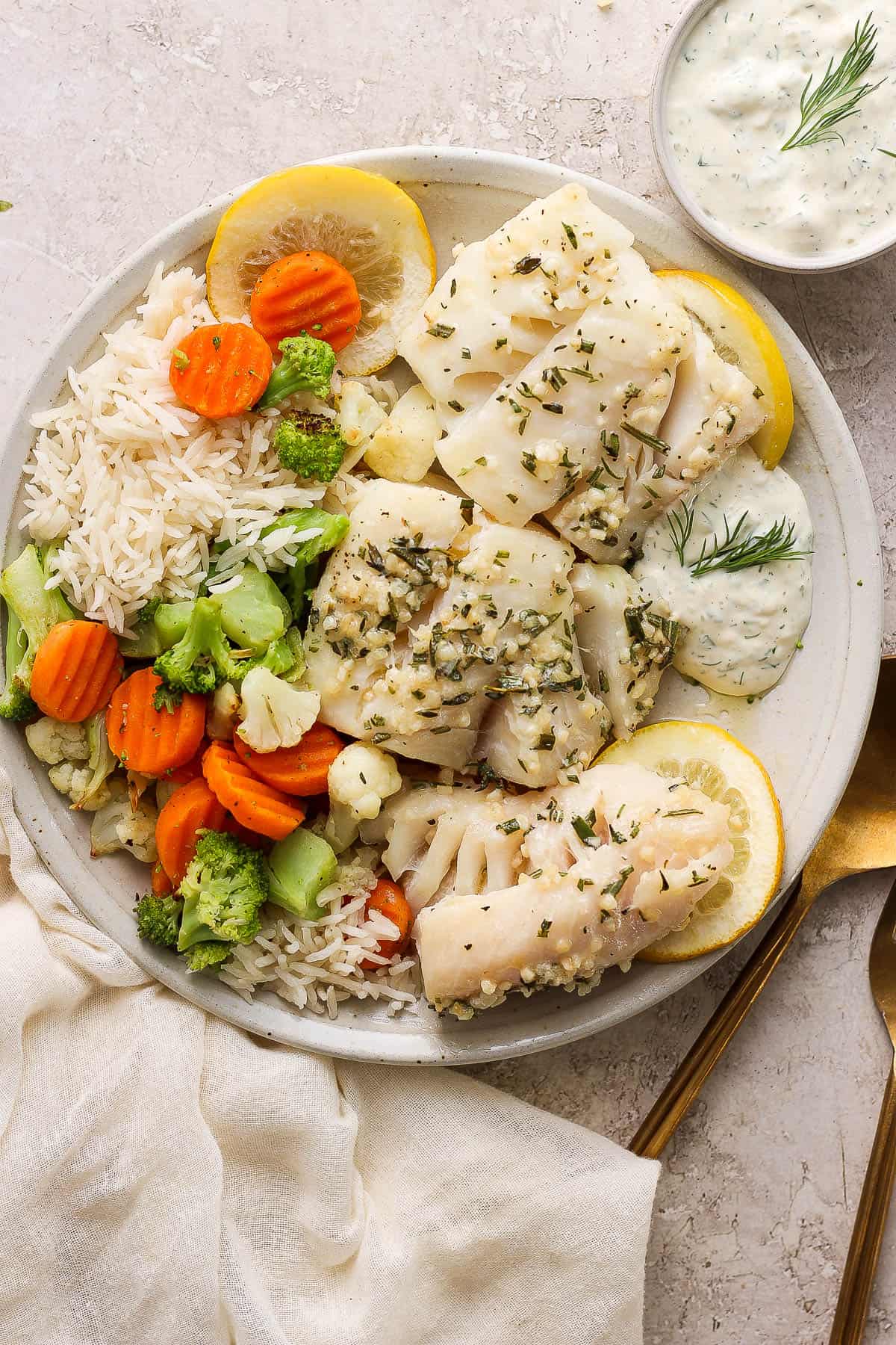 A dinner plate with baked cod, lemon slices, roasted veggies, and rice.