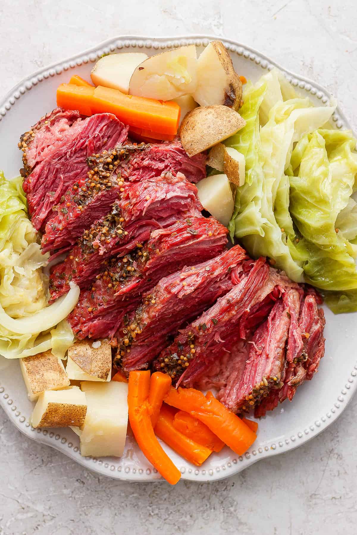 Corned beef sliced on a large white plate with some of the cooked veggies.
