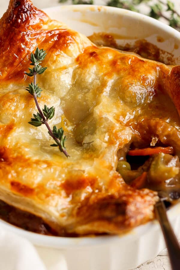 Side angle of a beef pot pie in a ramekin with puff pastry crust and a spoon sticking out.