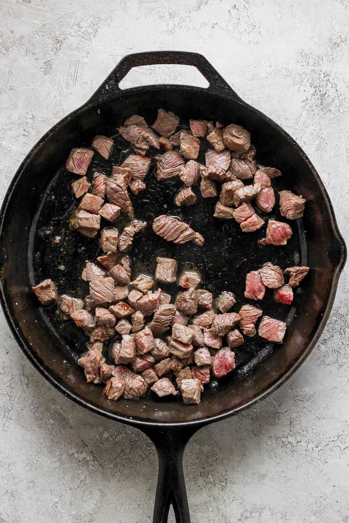 Cubed beef in a cast iron skillet getting seared on each side.