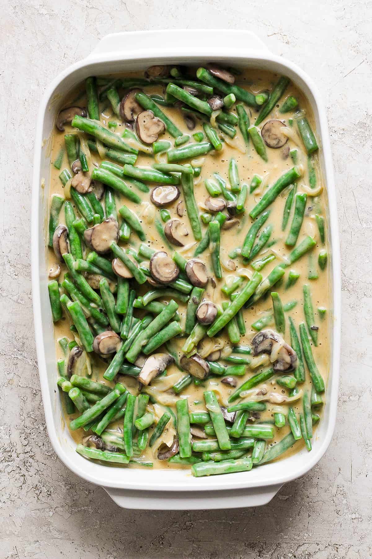 Green beans in a white baking dish with the mushroom mixture mixed in.