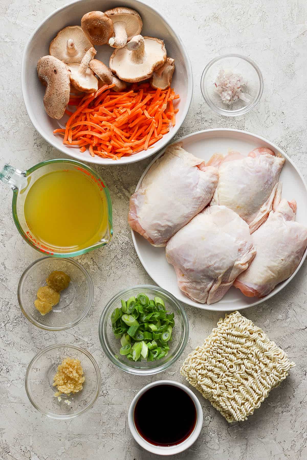 Ingredients for chicken ramen in separate bowls and plates.