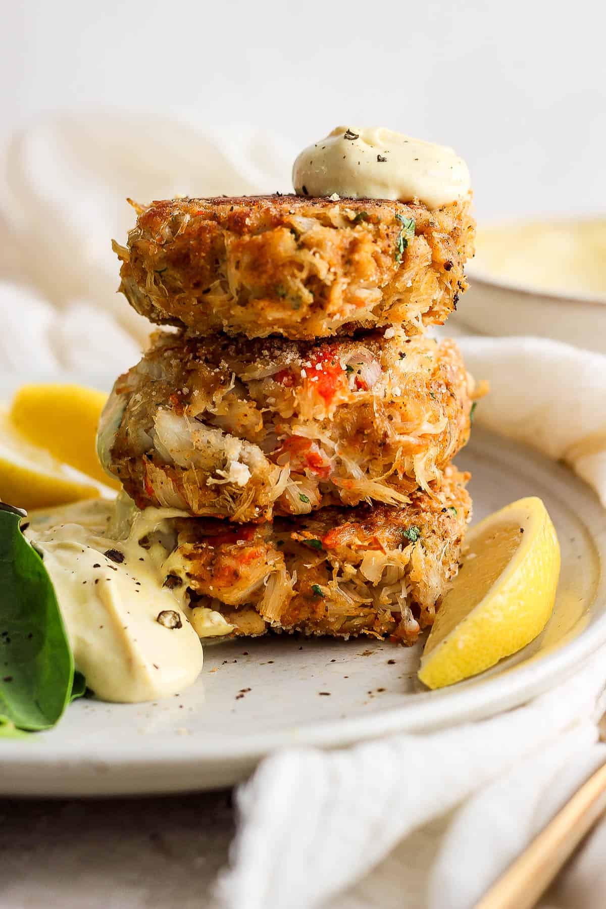 Three crab cakes stacked on top of each other with a dollop of crab cake sauce on the top and on the side.