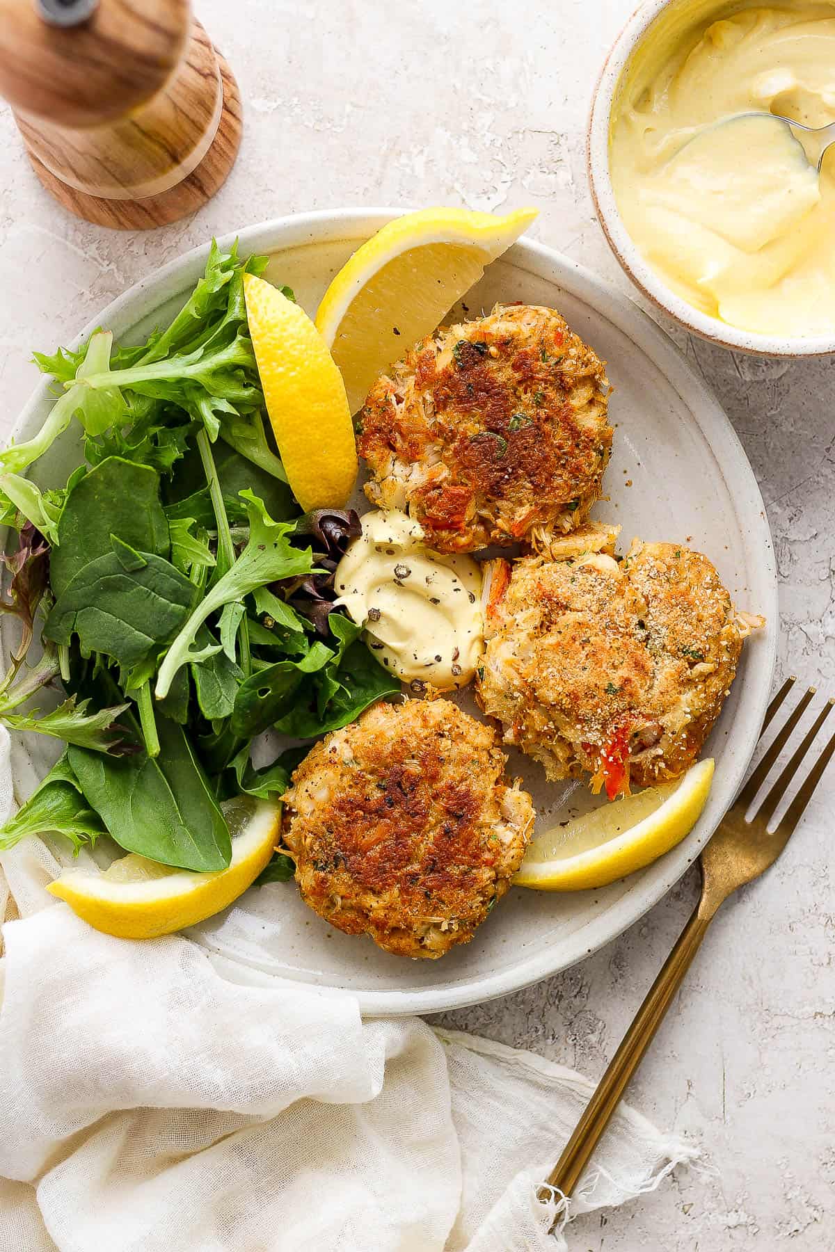 A plate of baked crab cakes with some salad and lemon wedges.