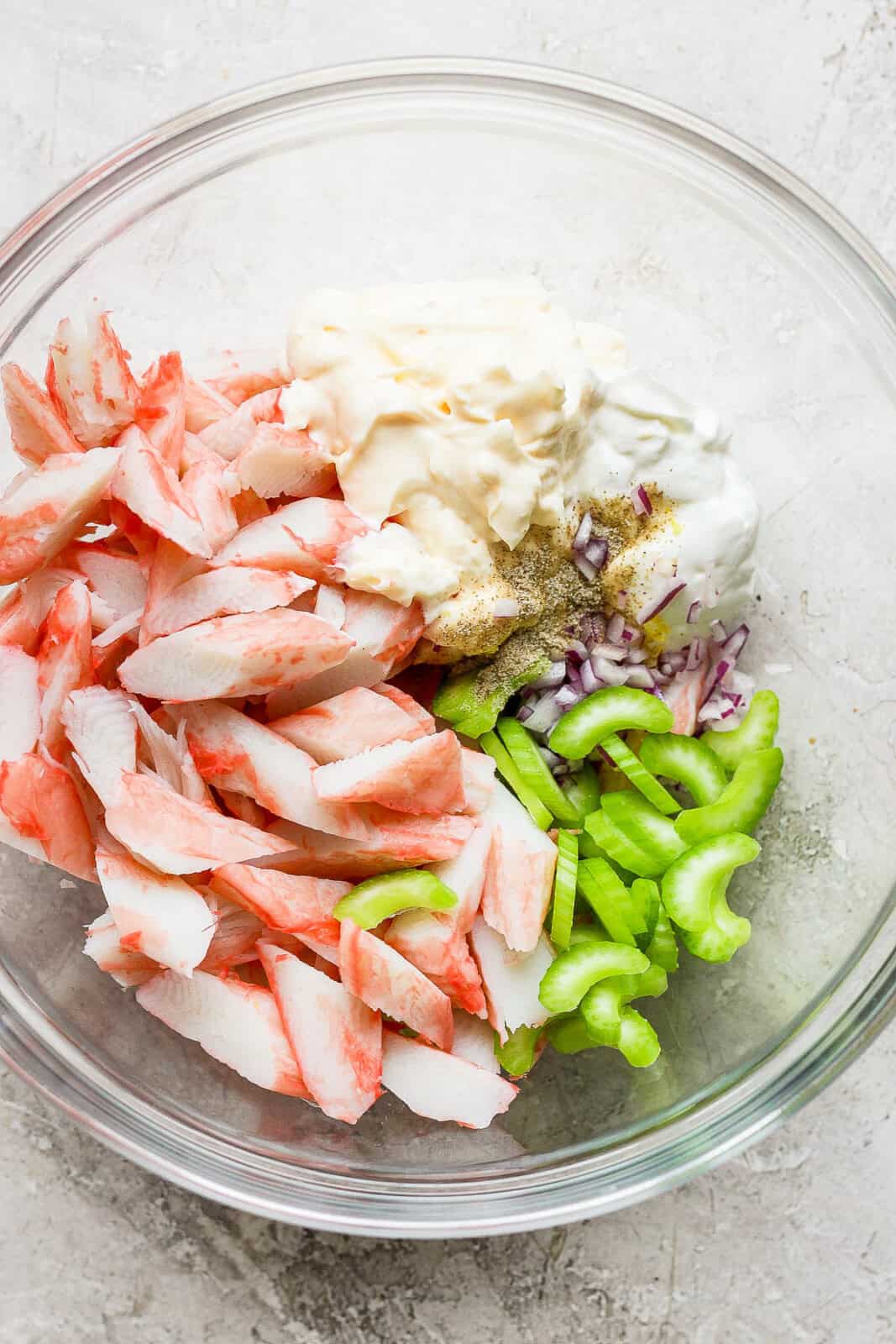 Crab salad ingredients in a glass bowl before mixing.