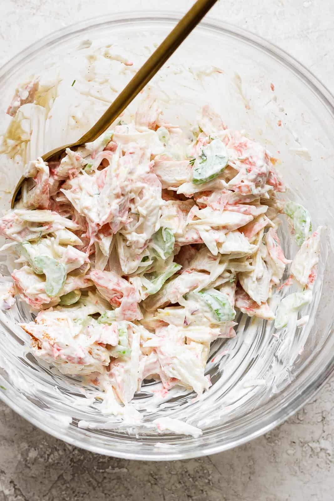 Crab salad in a glass bowl mixed with a spoon sticking out.