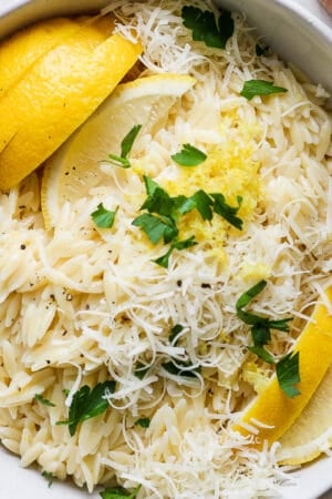 Top down shot of a bowl of lemon orzo with fresh lemon slices and parsley on top.