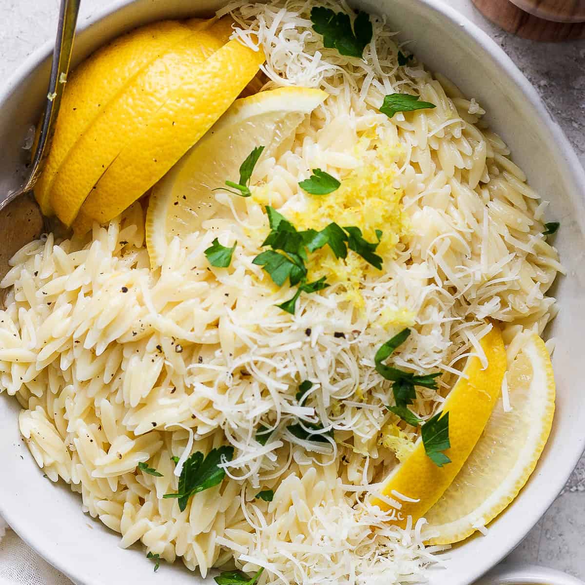 Top down shot of a bowl of lemon orzo with fresh lemon slices and parsley on top.