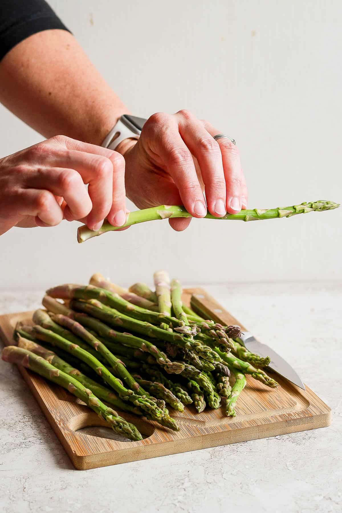Two hands holding one piece of asparagus.