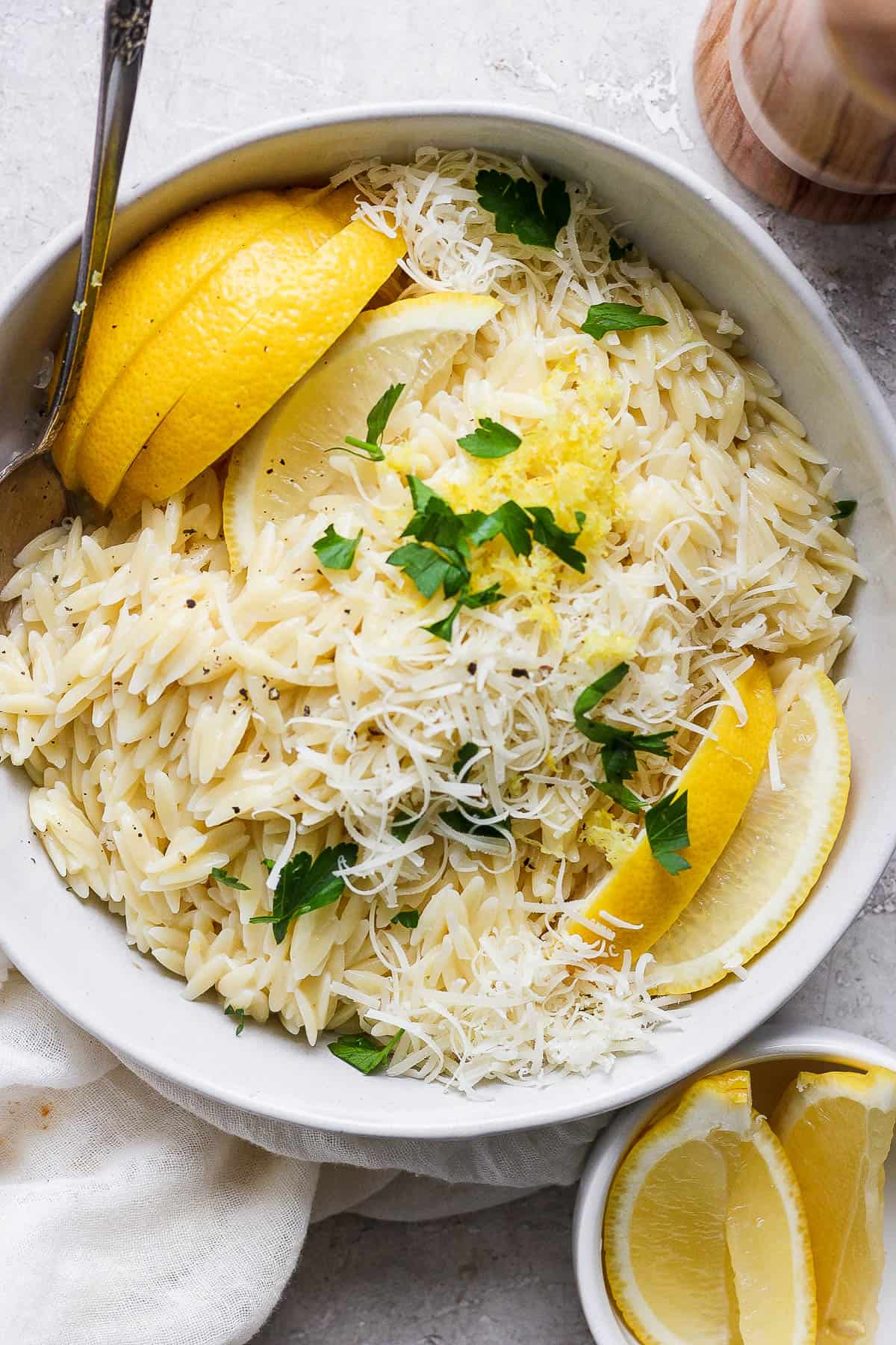 Lemon orzo in a bowl garnished with lemon wedges, shaved parmesan, lemon zest, and chopped parsley.