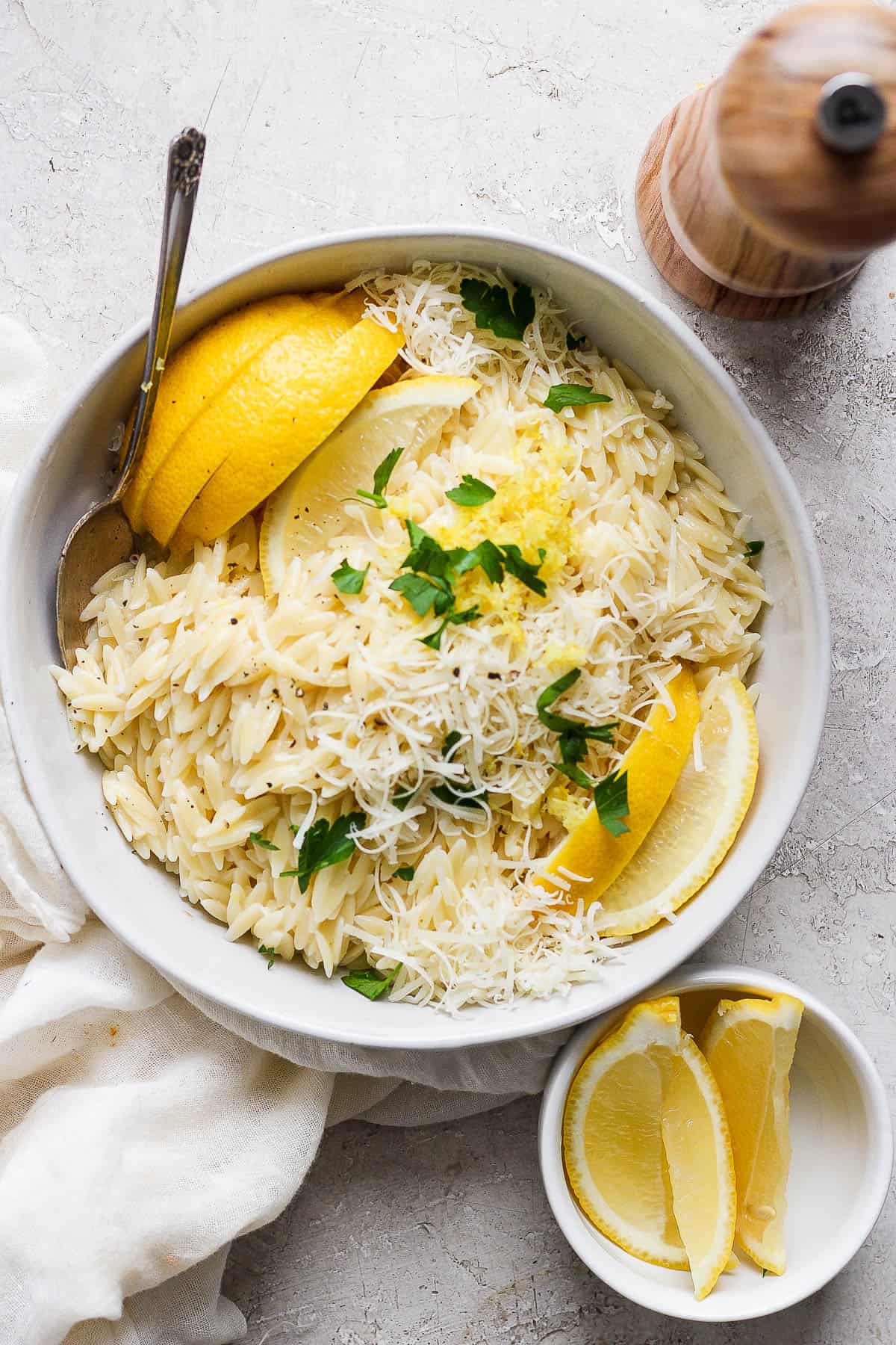 Lemon orzo in a bowl garnished with lemon wedges, shaved parmesan, lemon zest, and chopped parsley.