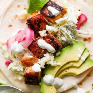 Top down shot of a salmon taco on a soft tortilla with pickled onions, avocado and cilantro lime crema drizzled on top.