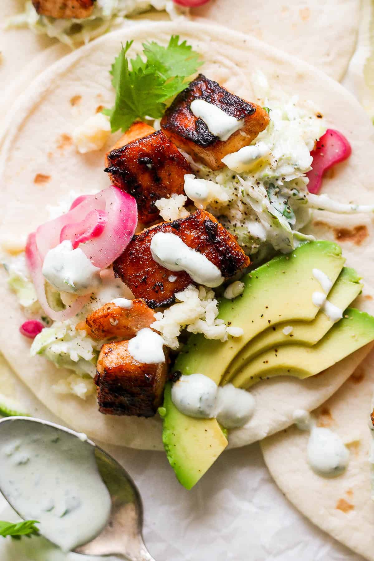 A salmon taco with cream topping and sliced avocado. 