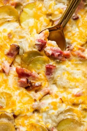 Top down shot of a pan of scalloped ham and potatoes with a spoon sticking out.
