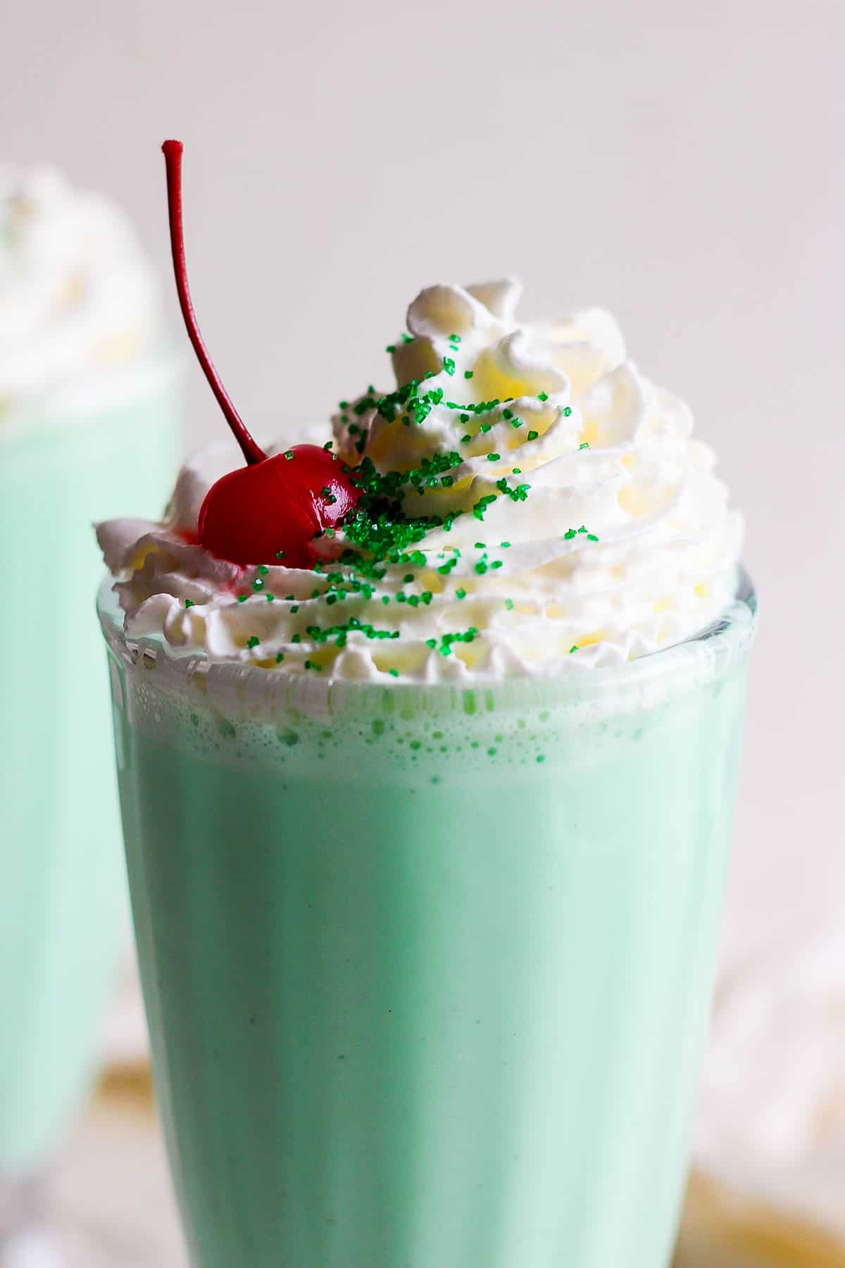 A shamrock shake topped with whipped cream, green sprinkles, and a cherry.