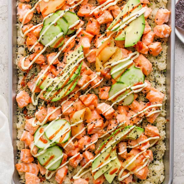 Top down shot of a pan of sushi bake with rice, cooked salmon, avocado and drizzled spicy mayo.