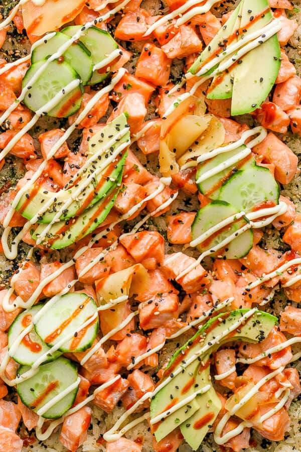 Top down shot of a pan of sushi bake with rice, cooked salmon, avocado and drizzled spicy mayo.