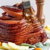 A side shot of a spiral ham with someone brushing a 3 ingredient glaze over it with a small brush.