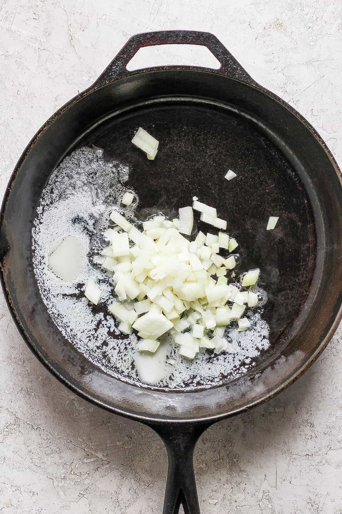 Butter melting in a cast iron skillet with chopped onions added.