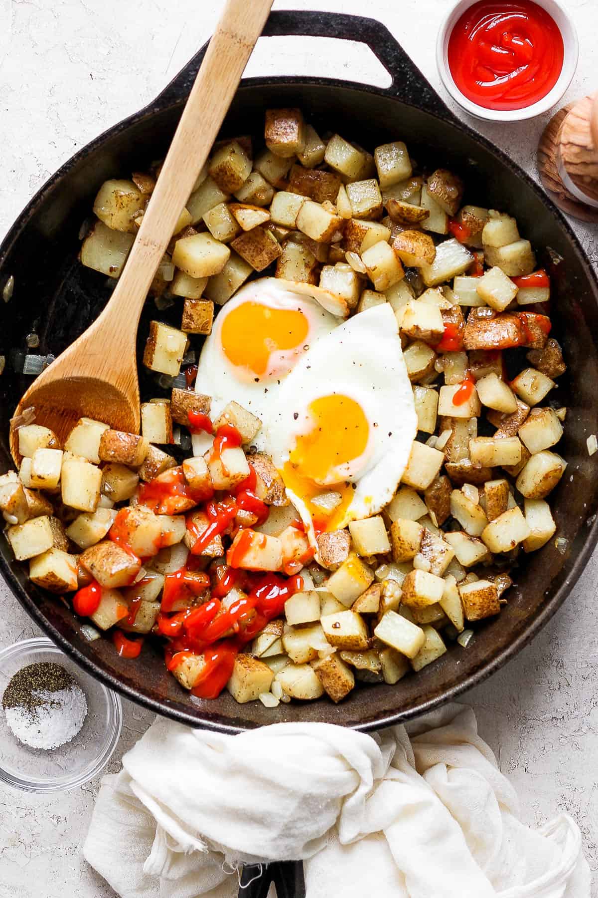 American fries in a skillet with two over easy eggs and ketchup.