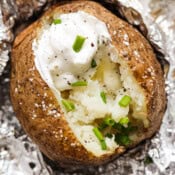 Top down shot of a grilled baked potato cut open with sour cream, butter, chives and pepper.