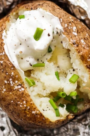 Top down shot of a grilled baked potato cut open with sour cream, butter, chives and pepper.