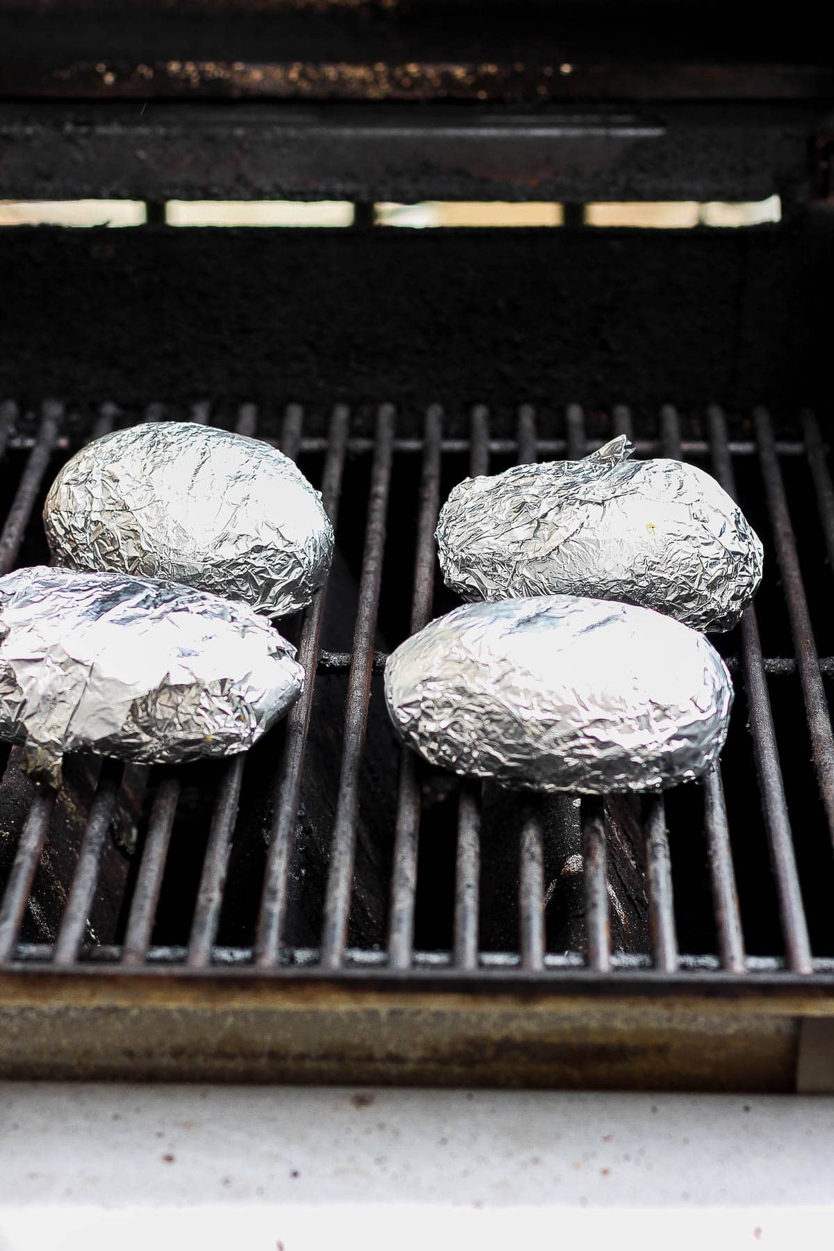Four wrapped potatoes on the grill grates.