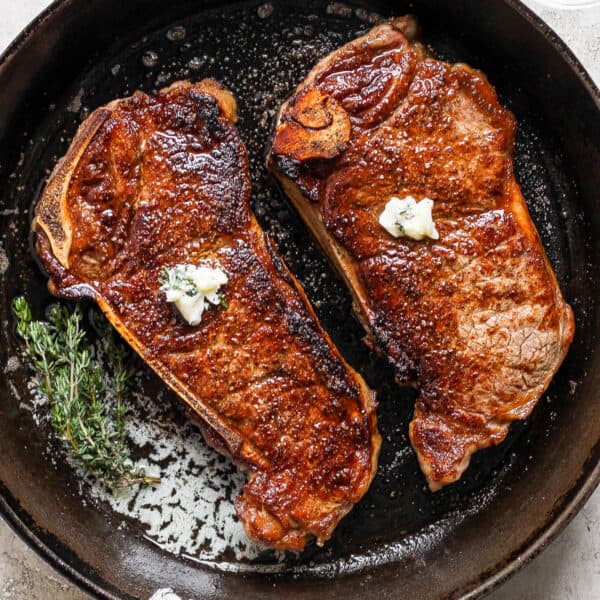 Top down shot of two new york strip steaks cooking in a cast iron skillet with melted butter and fresh thyme.