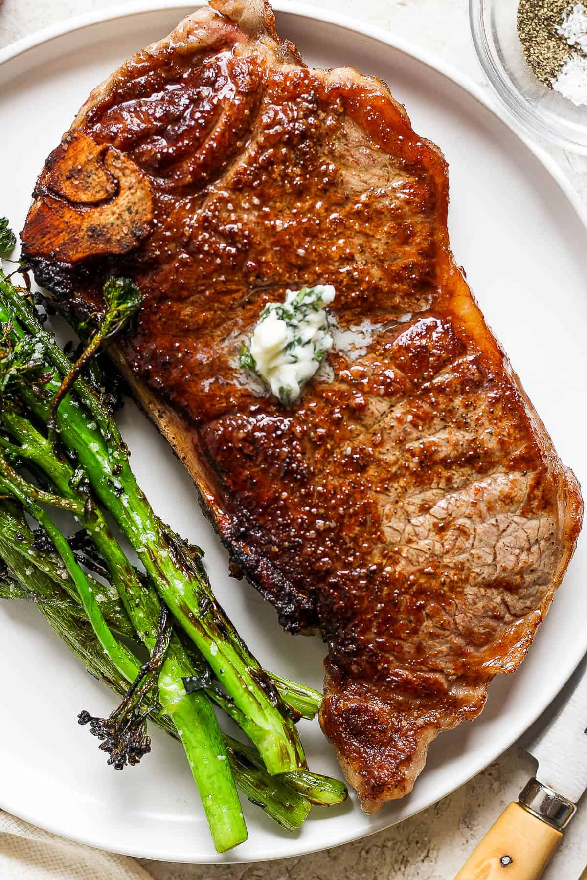 A perfectly cooked new york strip steak on a white plate with broccolini.
