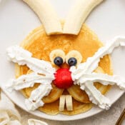 Top down shot of a pancakes, banana, blueberries, strawberries and whipped cream in the shape of a bunny.
