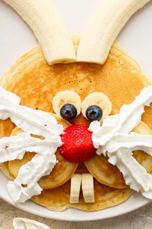 Top down shot of a pancakes, banana, blueberries, strawberries and whipped cream in the shape of a bunny.