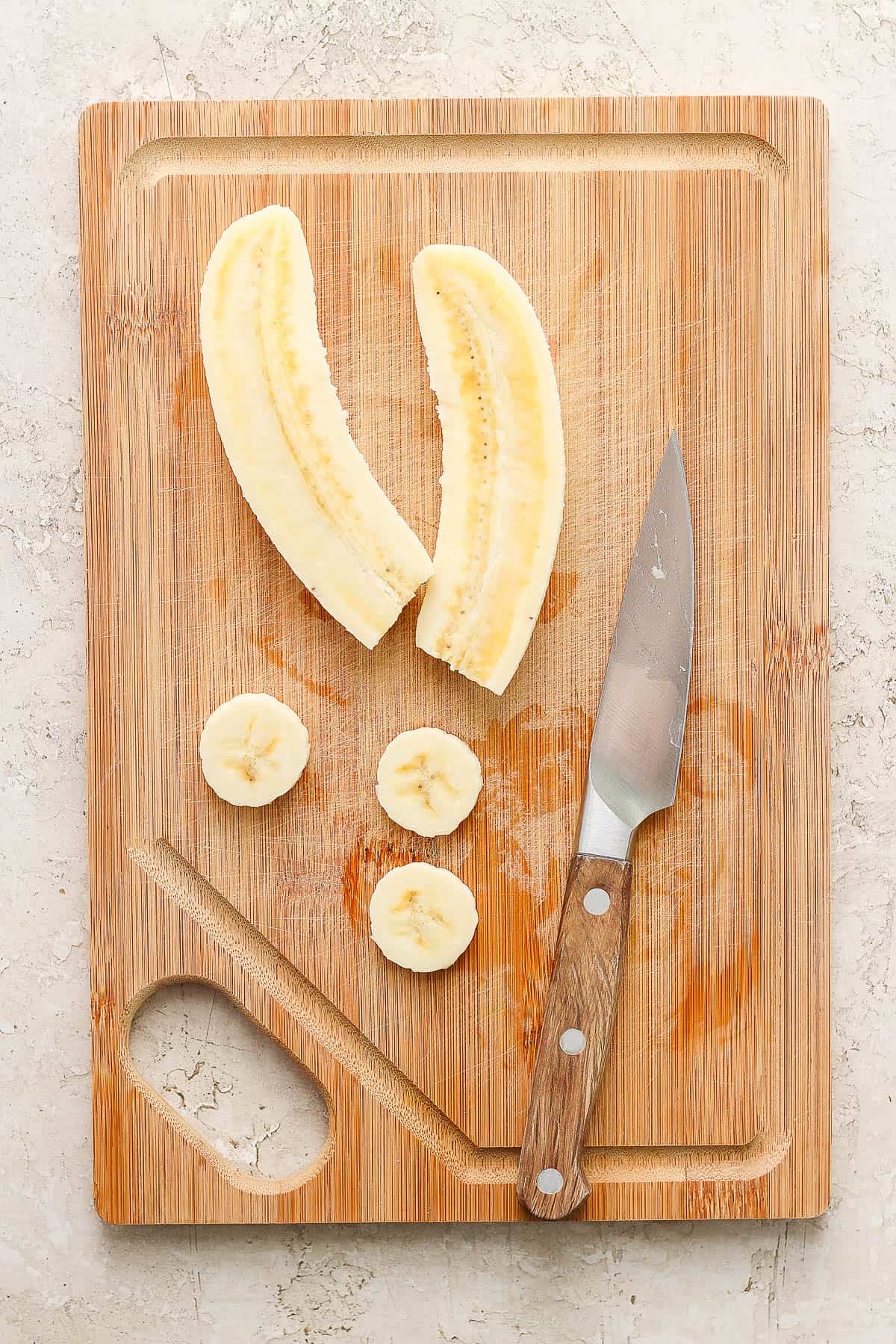 A peeled banana being cut on a cutting board.