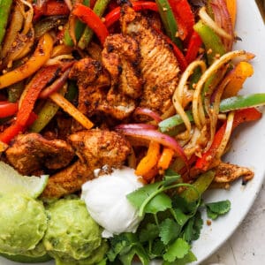 Top down shot of a platter of grilled chicken fajitas with veggies, sour cream and guacamole.