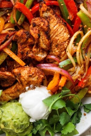 Top down shot of a platter of grilled chicken fajitas with veggies, sour cream and guacamole.
