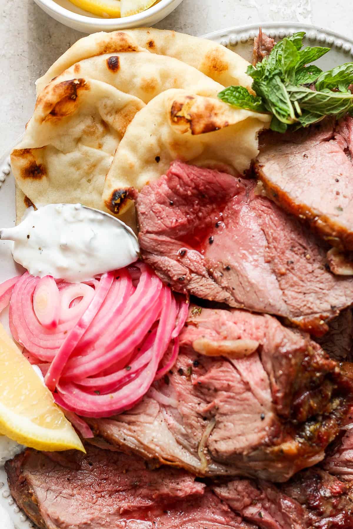 Close-up shot of lamb slices on a plate with a spoon of sauce.