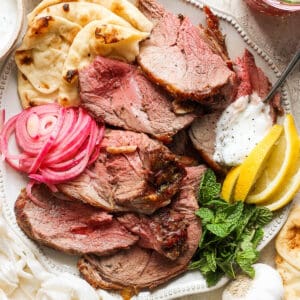 Top down shot of a plate of grilled lamb leg with pickled onions, mint, lemon wedges and pita.
