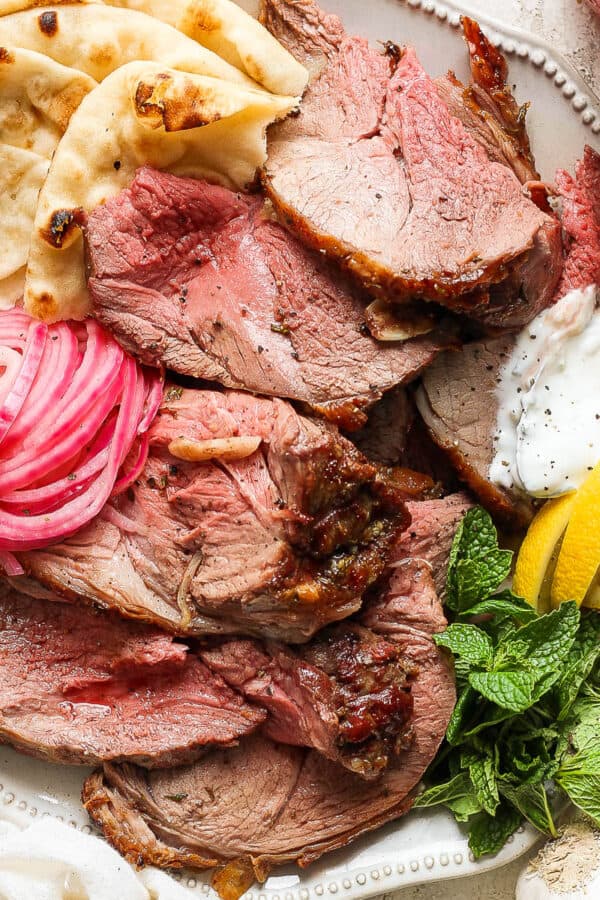 Top down shot of a plate of grilled lamb leg with pickled onions, mint, lemon wedges and pita.
