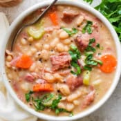 Top down shot of a bowl of ham bean soup with a spoon sticking out and garnished with fresh parsley.