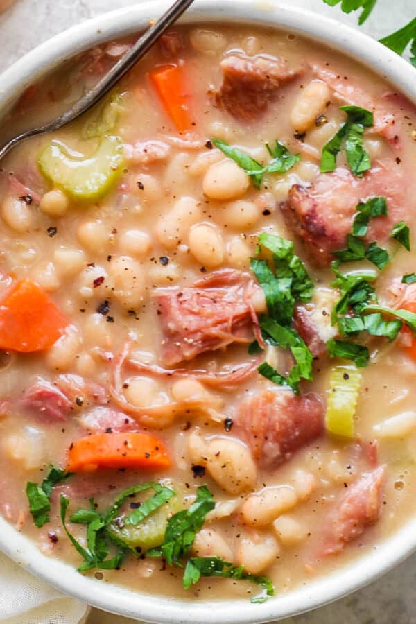 Top down shot of a bowl of ham bean soup with a spoon sticking out and garnished with fresh parsley.